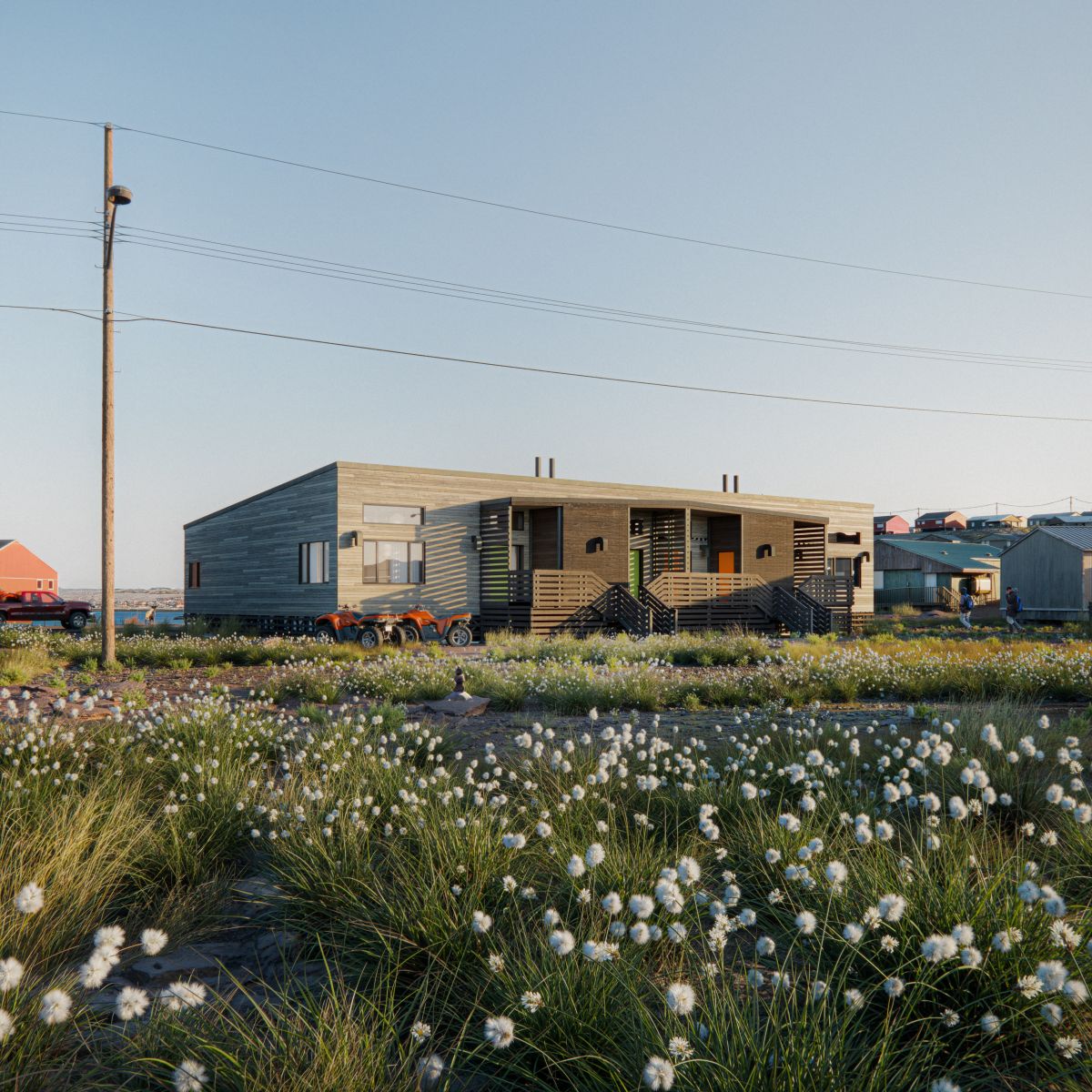 Rendu 3D d’un immeuble de maisons en rangée doté d’un toit plat, d’une façade en panneaux de bois et d’entrées en retrait. L'immeuble comprend des porches couverts, des garde-corps à lattes horizontales et des escaliers menant à chaque logement. Il se situe au cœur d’un paysage ouvert à côté de bâtiments voisins.